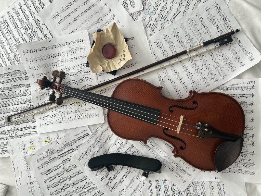 Violin, shoulder rest, rosin, and violin bow on top of sheet music