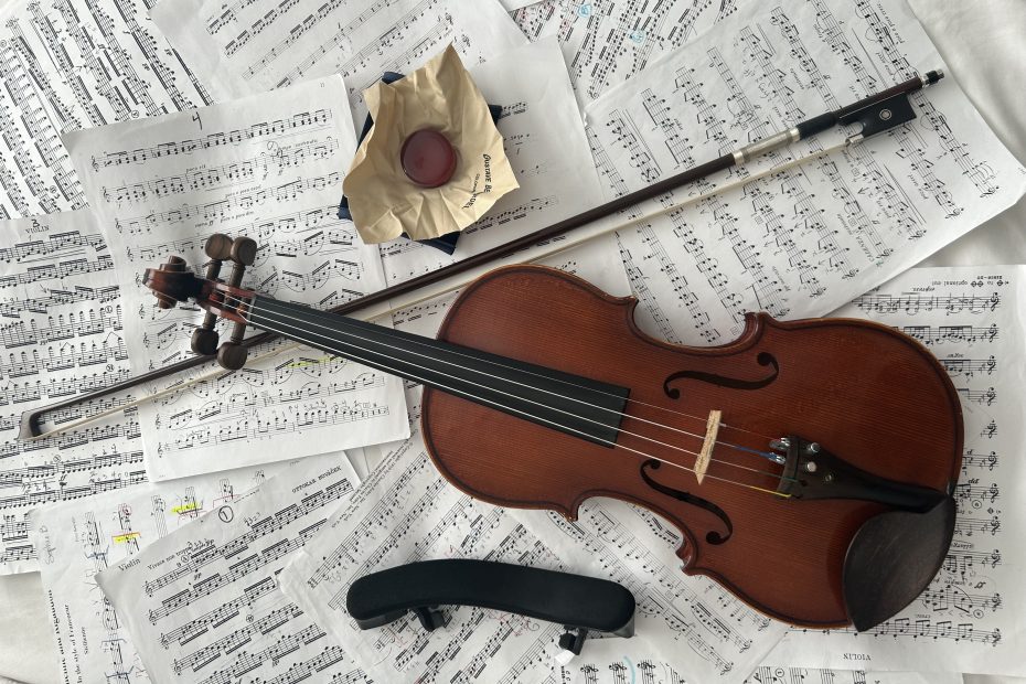 Violin, shoulder rest, rosin, and violin bow on top of sheet music